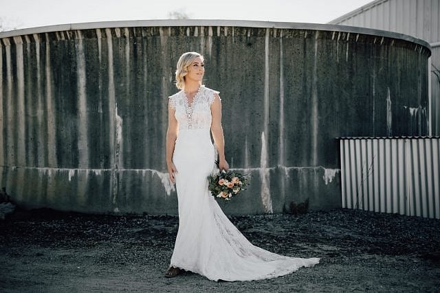 Bride Stand outside near a water tank in the background creating a beautiful textural backdrop